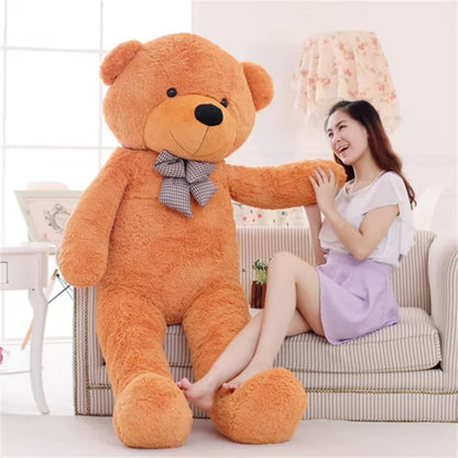 Giant light brown teddy bear with a plaid bow, sitting on a sofa next to an adult for scale