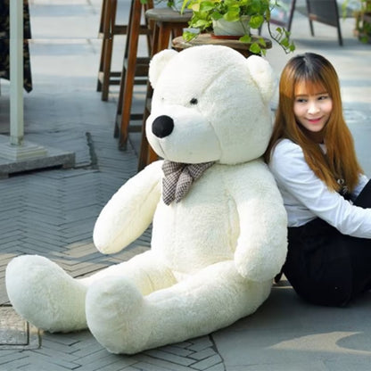 Giant white teddy bear with a plaid bow sitting outdoors next to a woman